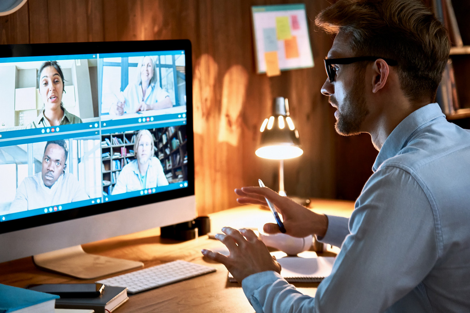 A man working from home, having a virtual meeting with four other people, on his desktop computer